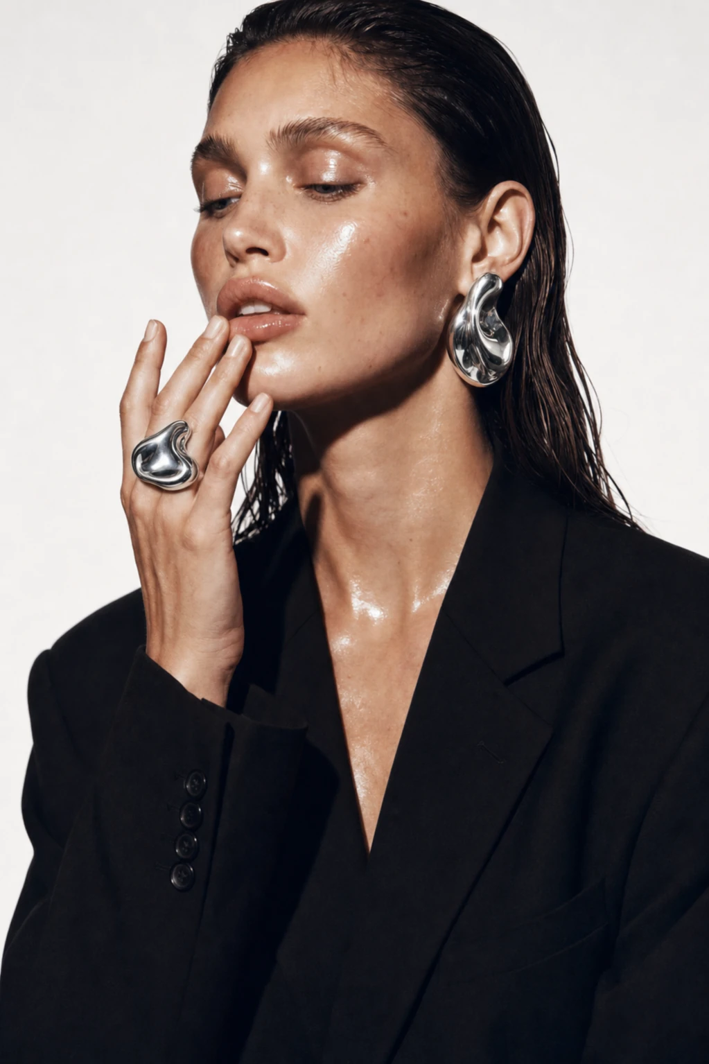 Model touching her lips, wearing a sculptural silver ring and earring