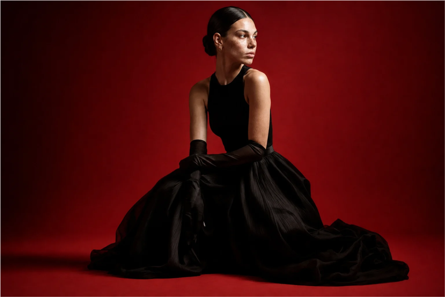 Seated black gown campaign portrait against a red backdrop